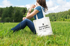 White tote bag with top handles and printed slogan, carried while seated outdoors
