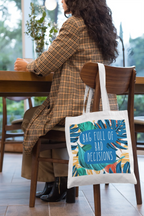 White tote bag hanging from shoulder, featuring tropical leaves and teal circular text.