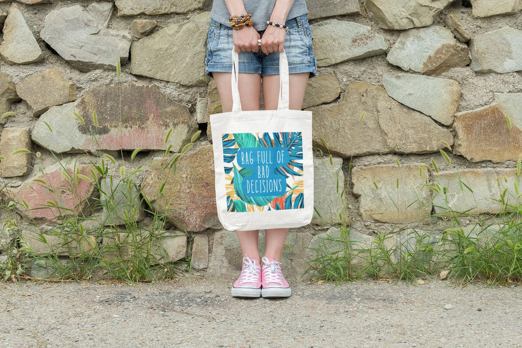 White canvas tote bag with tropical print and teal circular lettering on front.