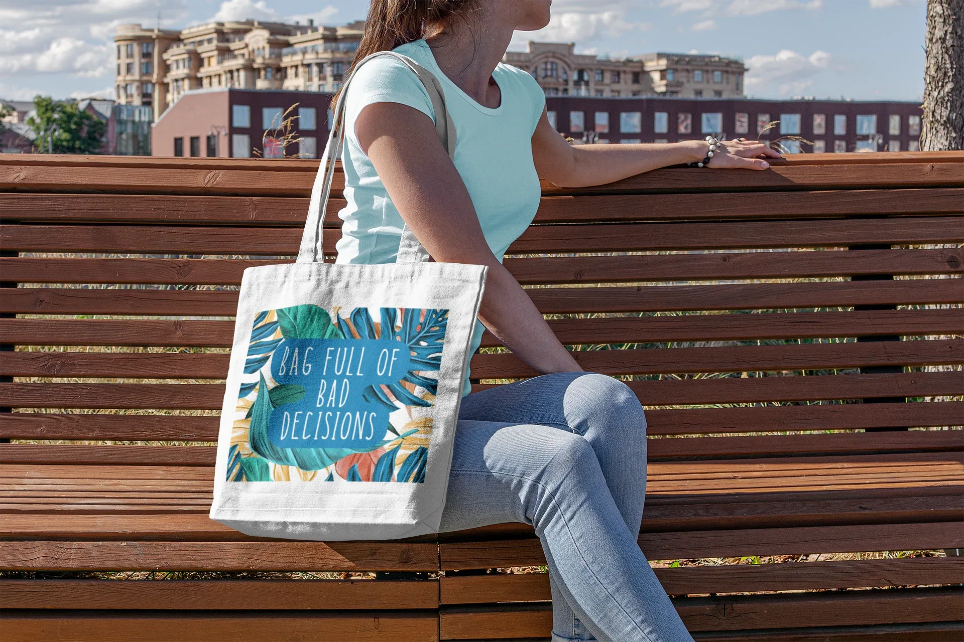 White canvas tote bag with tropical leaf graphic and teal “bad decisions” text.
