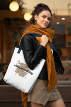 White tote bag with brown 'Have a great day' print, carried by person on shoulder