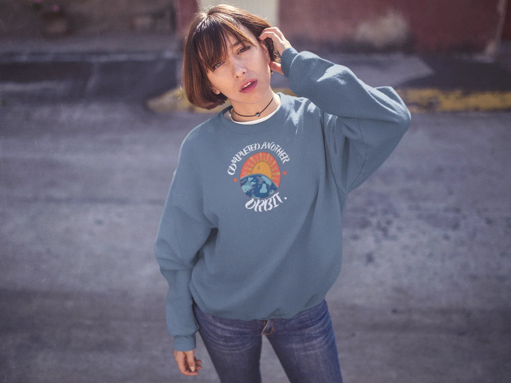 Light blue crewneck sweatshirt with space graphic logo at center chest.