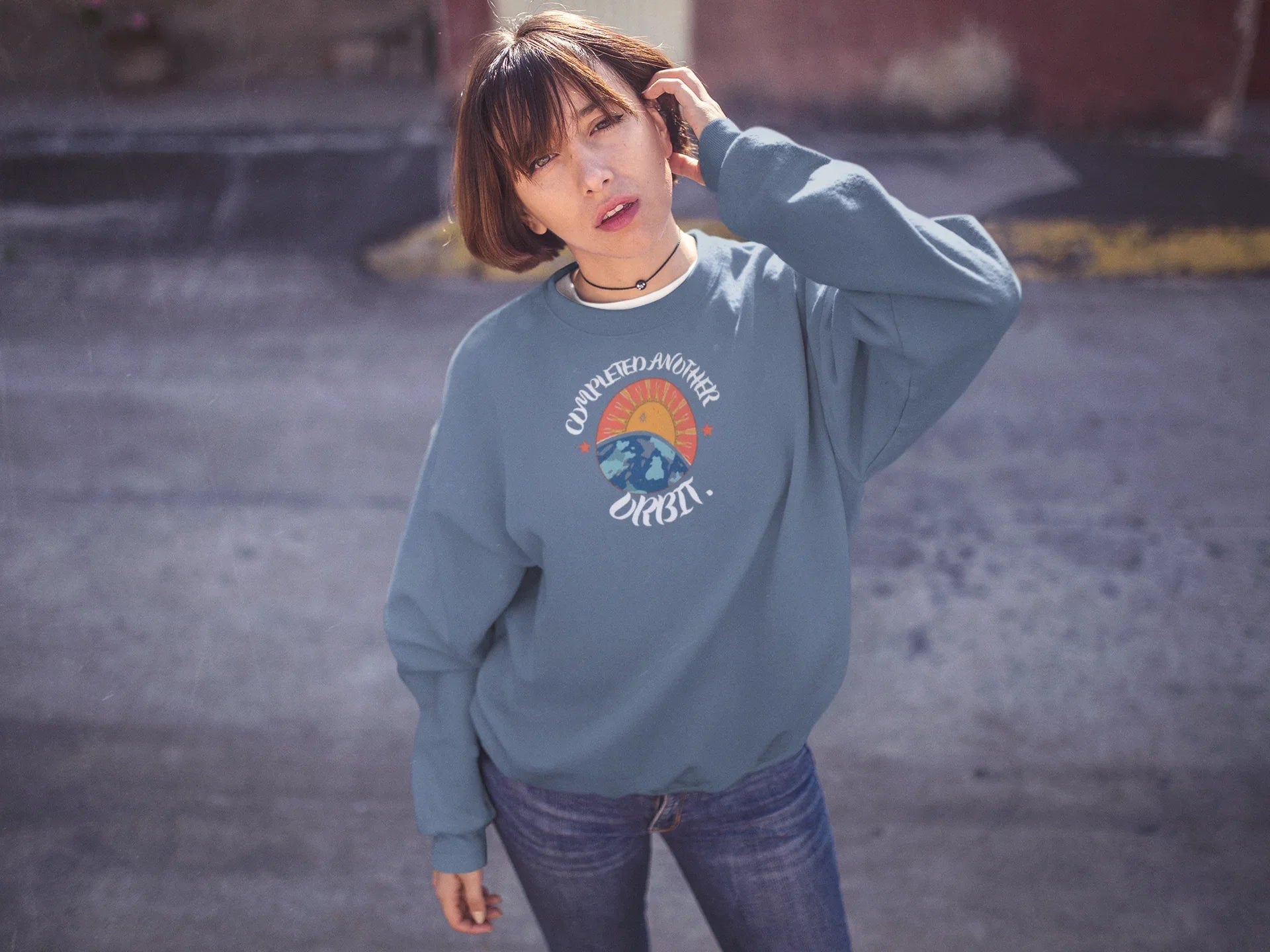 Light blue crewneck sweatshirt with space graphic logo at center chest.