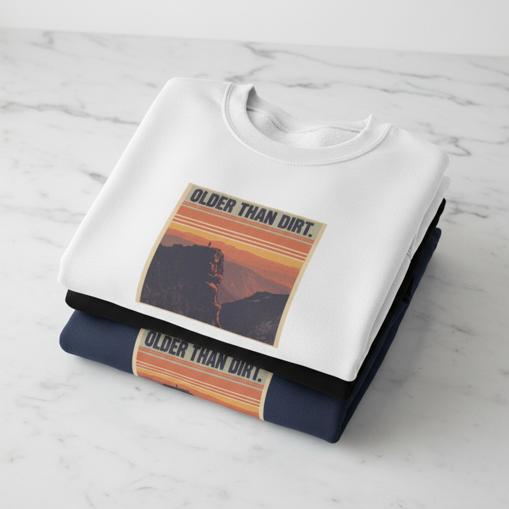 White crewneck sweatshirt with mountain sunset graphic, folded with dark shirt beneath