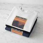 White crewneck sweatshirt with mountain sunset graphic, folded with dark shirt beneath