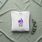 White hoodie folded on fabric with drawstring hood and purple “TRUST GOD’S PLAN” design.