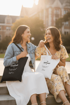 Two people holding graduation tote bags: black for Sophie and white for Ella