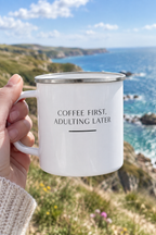 White enamel camping mug with 'Coffee first, adulting later' text, silver rim