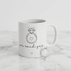 White ceramic mug with diamond ring graphic and 'we said yes' text, with ring beside