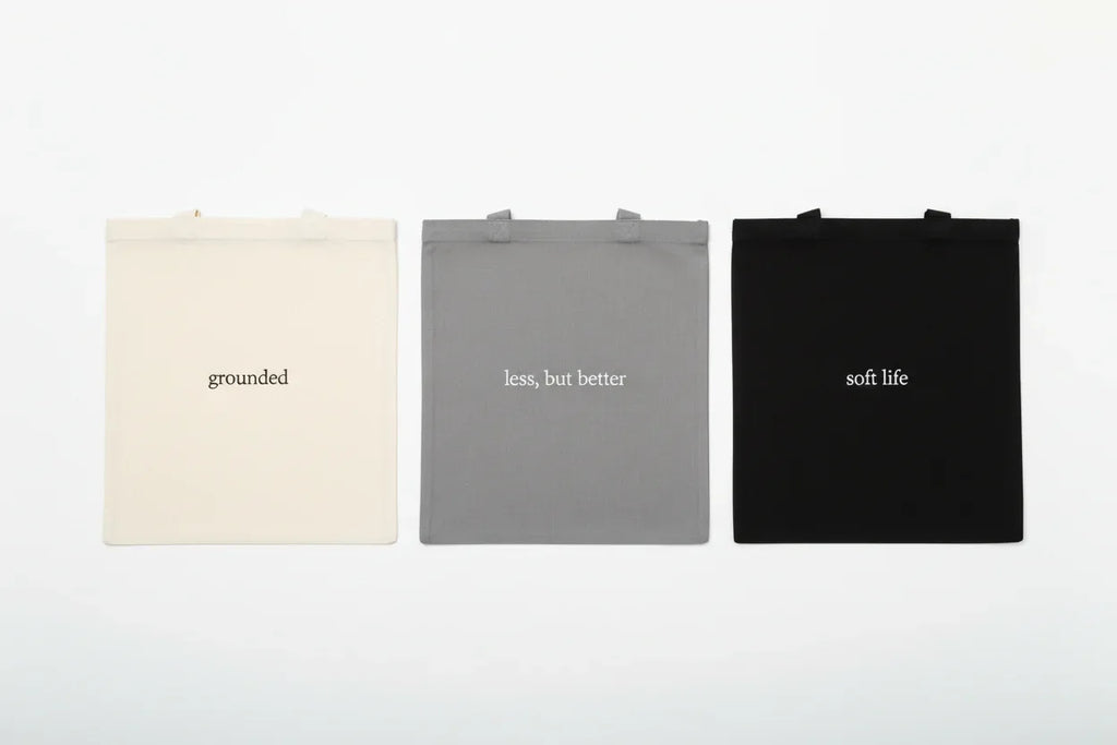 Three cotton tote bags: cream 'grounded', grey 'less, but better', black 'soft life'.