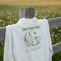 White hoodie close-up, back “Trust God’s Plan” moon and greenery graphic