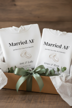 White hoodies with “Married AF” print, ring graphic, custom names; tied with green ribbon