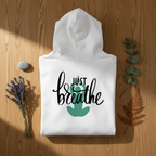 White hoodie with “Just breathe” slogan and hand heart graphic on back, folded