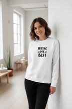 White sweatshirt with “TRYING MY BEST” quote print and green heart detail.