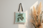 White tote bag with black handles and green monstera leaf print panel