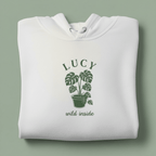 White hoodie with front hood and eyelet drawstrings; potted palm graphic with “LUCY”.