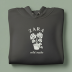 Dark gray hoodie with front hood and eyelet drawstrings; potted palm graphic with “ZARA”.