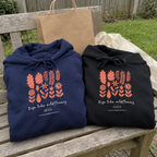 Wildflowers hoodies beside a gift bag in a garden