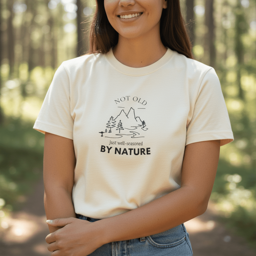 Ivory T-shirt with centered white mountain, trees, and 'BY NATURE' print